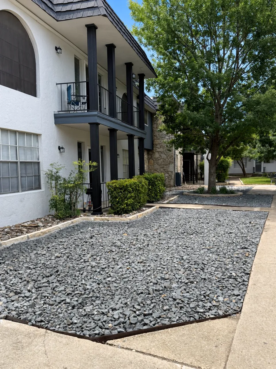 Tree-shaded courtyard with stone landscaping at Wilshire Woods Apartments